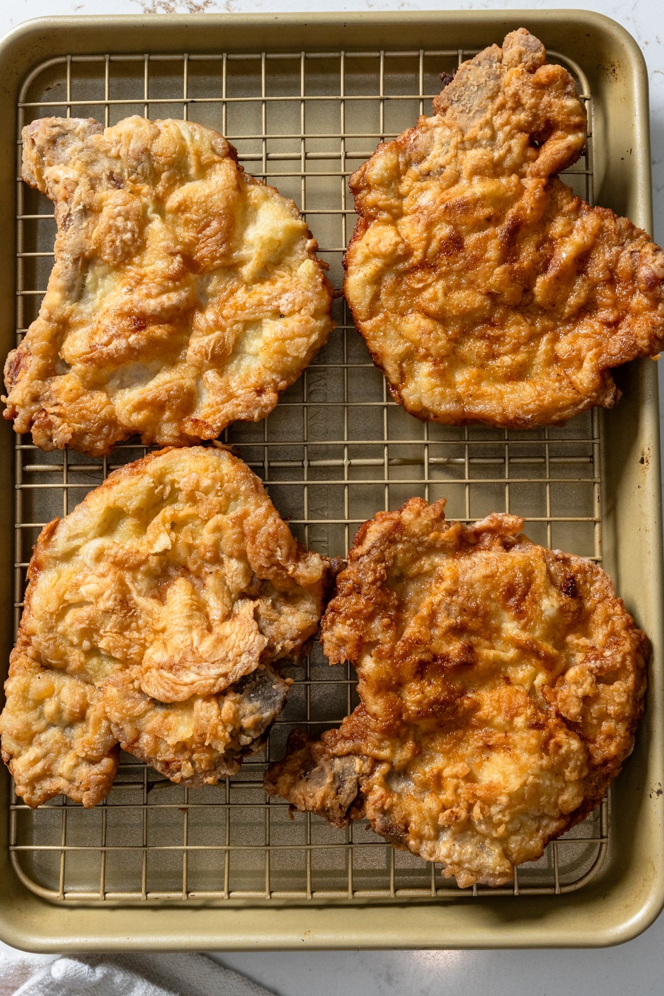 Four crispy fried pork chops on a wire cooling rack.