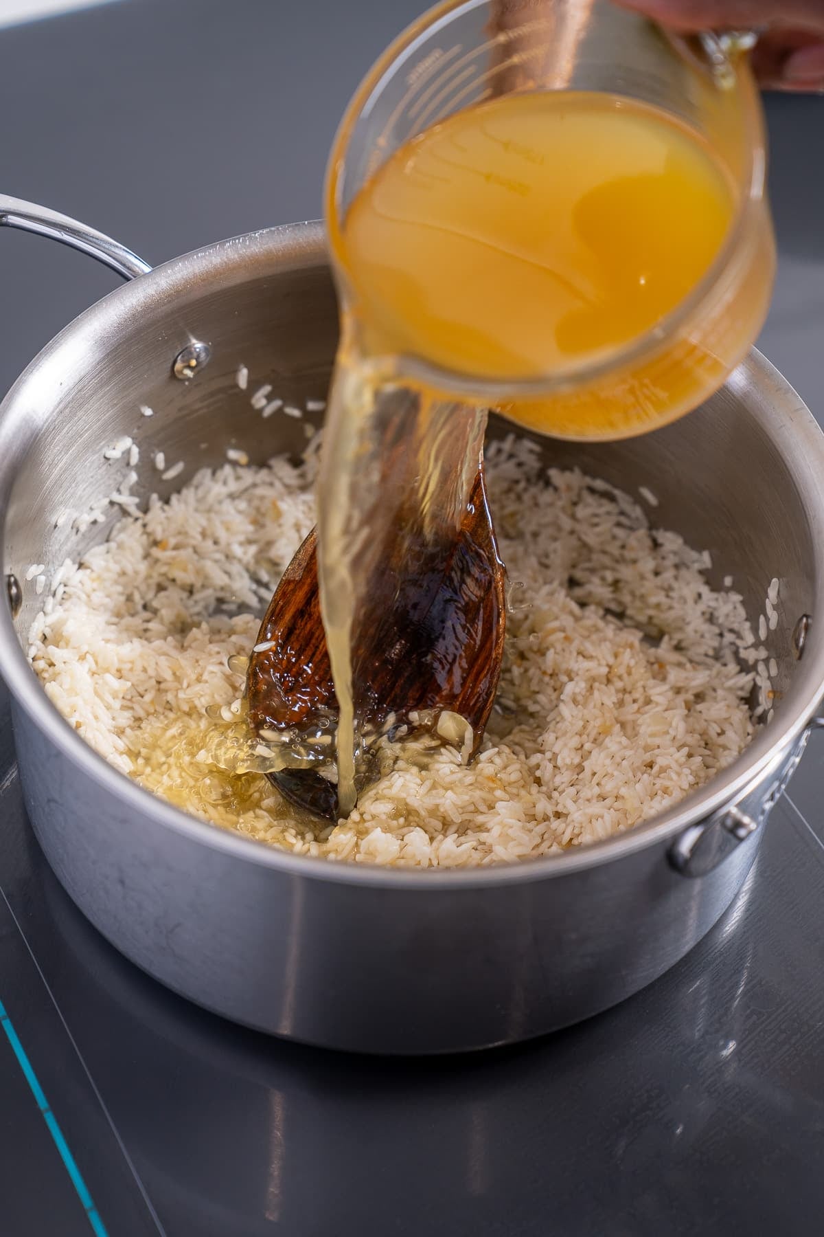 broth being poured into sauce pan along with the rice