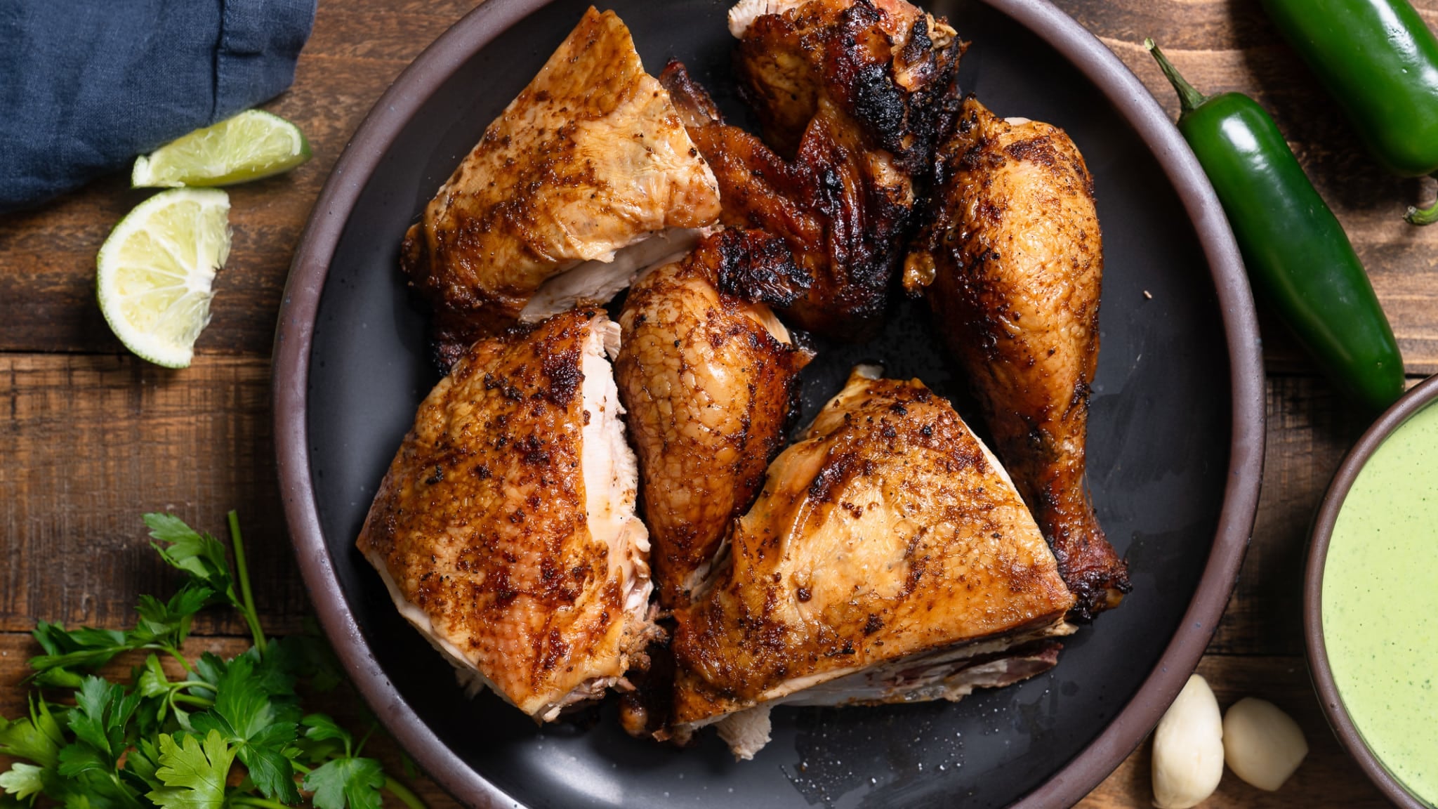 Peruvian chicken pieces cut up on plates, surrounded by jalapeno, cilantro, limes, and aji verde sauce.