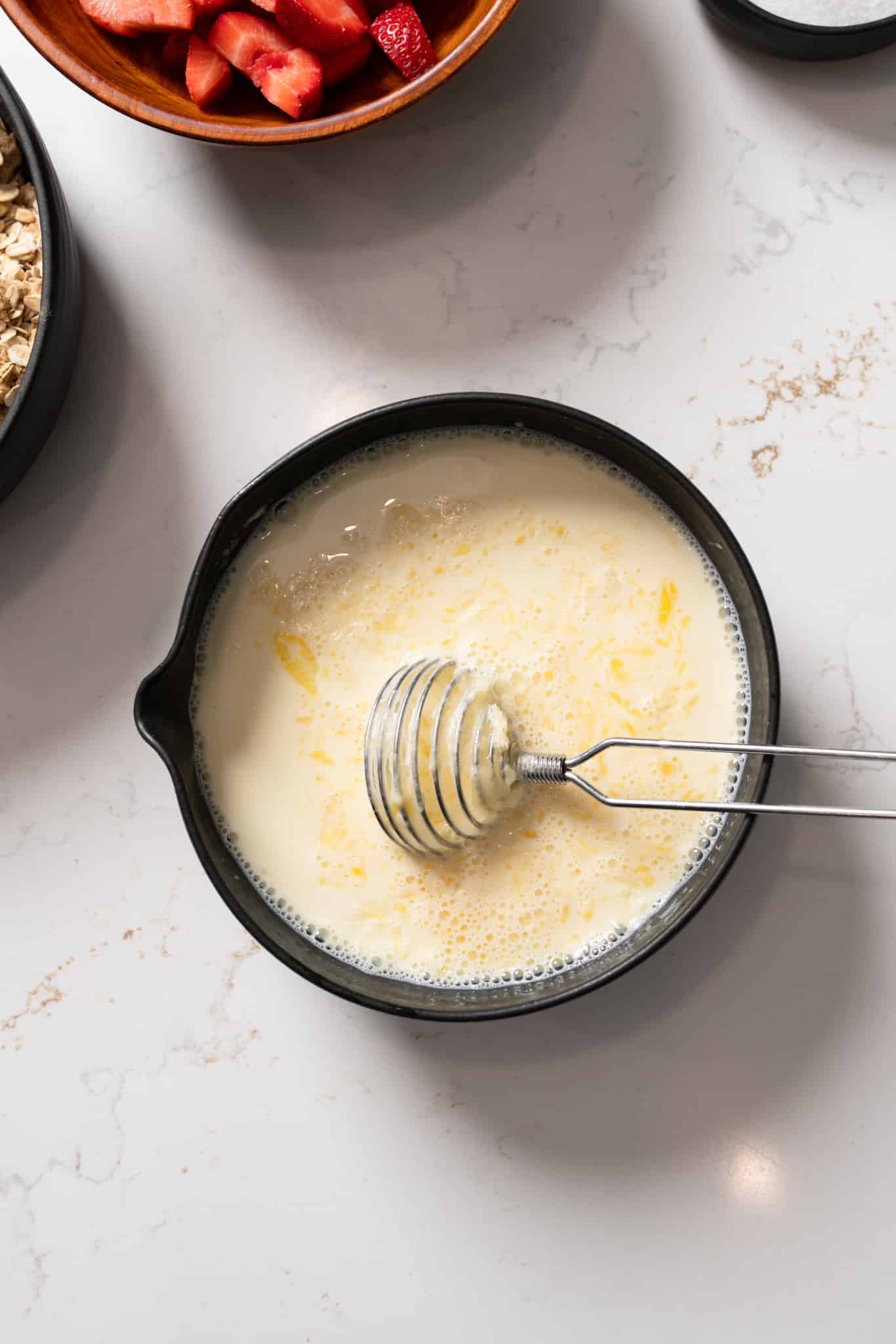 Milk and eggs mixed in a bowl with a whisk in it