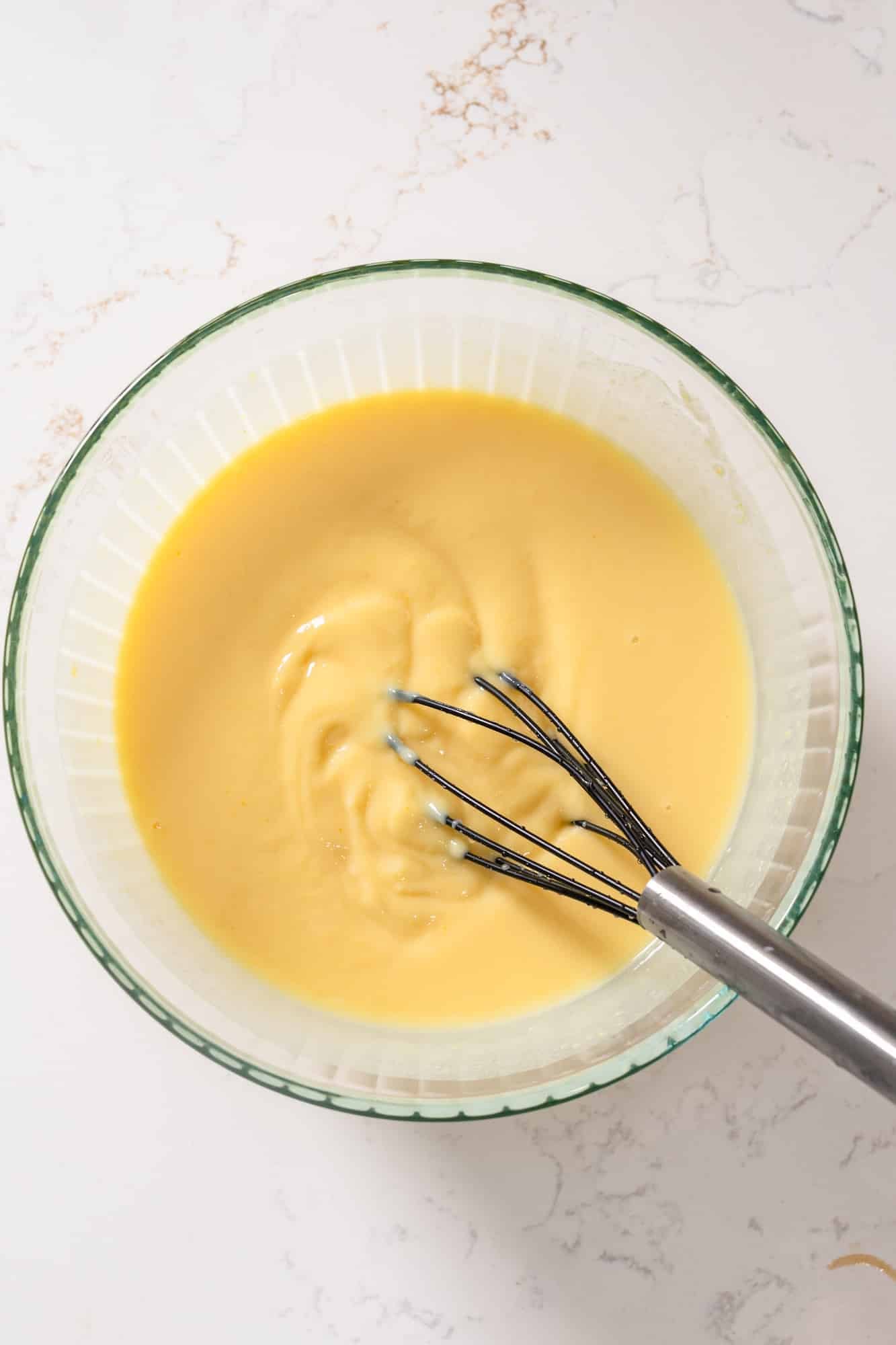 Vanilla pudding, condensed milk, and water being stirred with the whisk