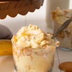 Banana pudding in a glass jar with a spoon sticking out and Nilla wafers surrounding the glass.