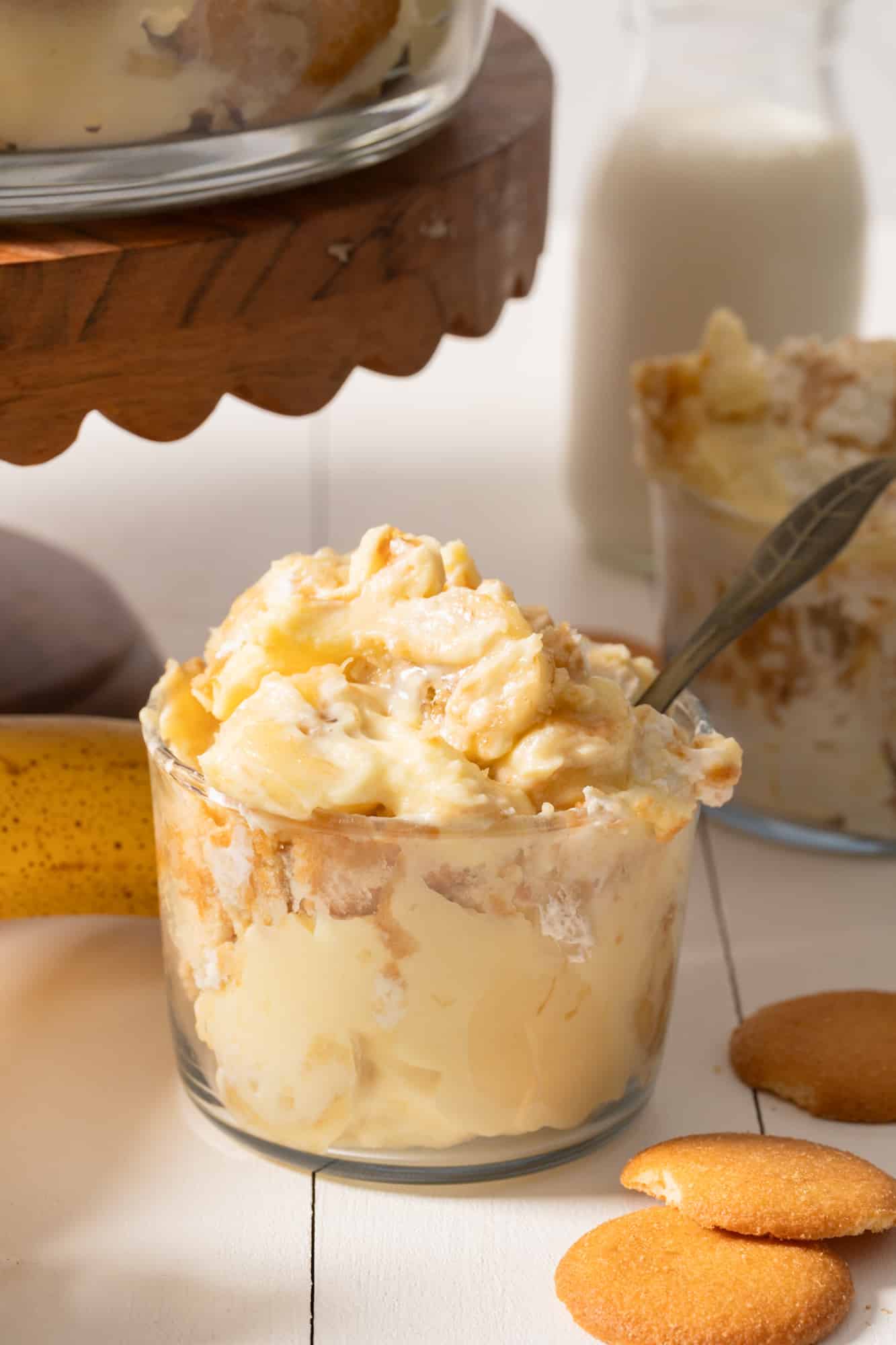 Banana pudding in a glass jar with a spoon sticking out and Nilla wafers surrounding the glass.