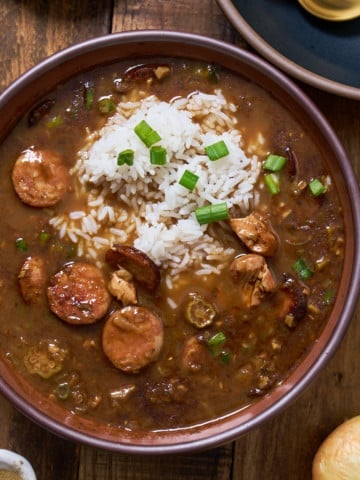 gumbo in a bowl with rice on top with green onions