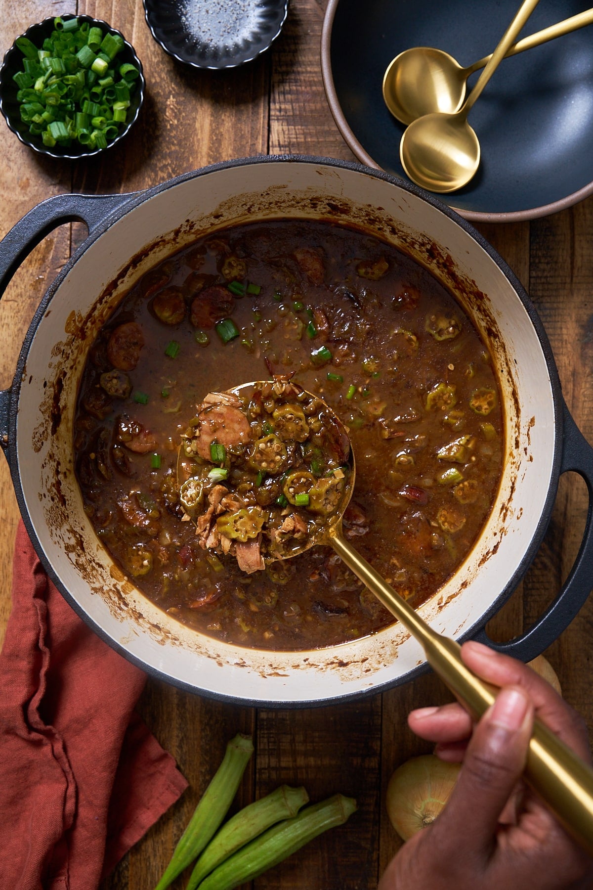 Hand holding spoon, picking gumbo out of pot