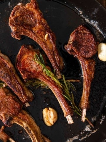 Lamb chops in skillet with rosemary and garlic.
