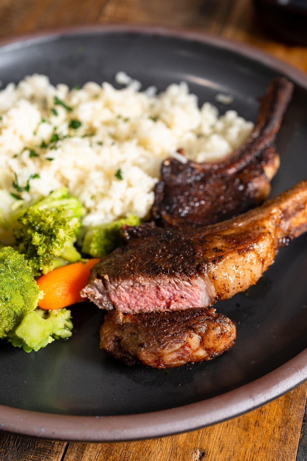 Cut lamb chops on a plate with rice and vegetables.