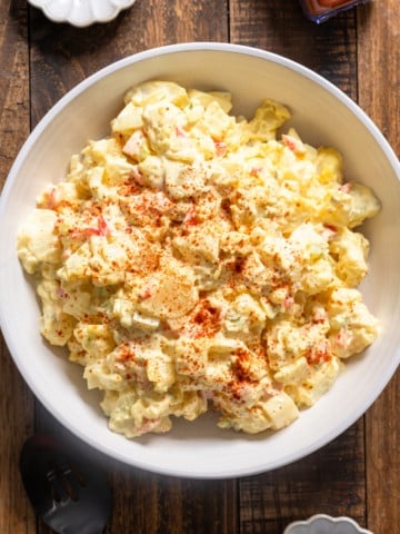 Potato salad in a white bowl on a wood table.