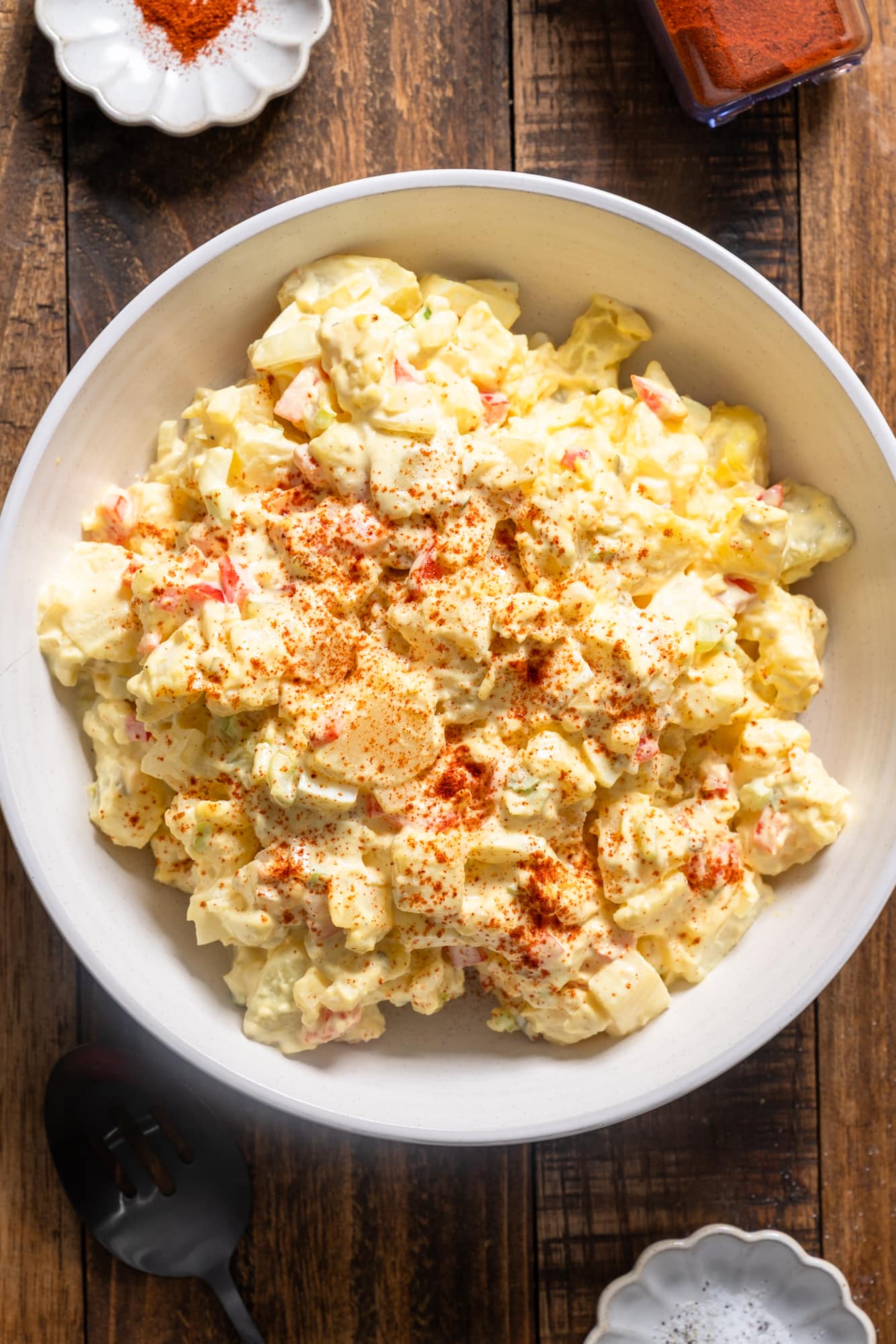 Potato salad in a white bowl on a wood table.