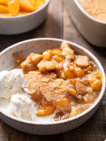 peach cobbler in a bowl with vanilla ice cream on the side