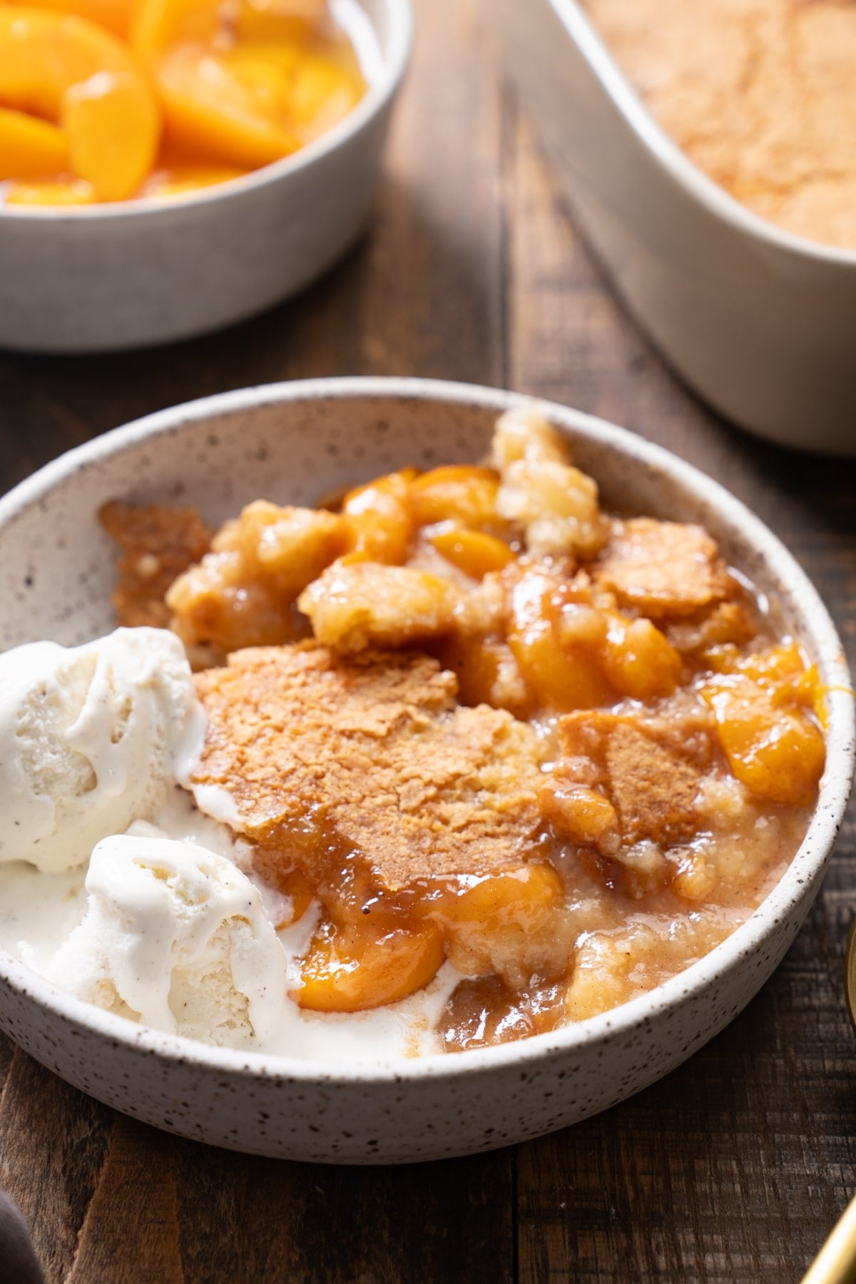 peach cobbler in a bowl with vanilla ice cream on the side