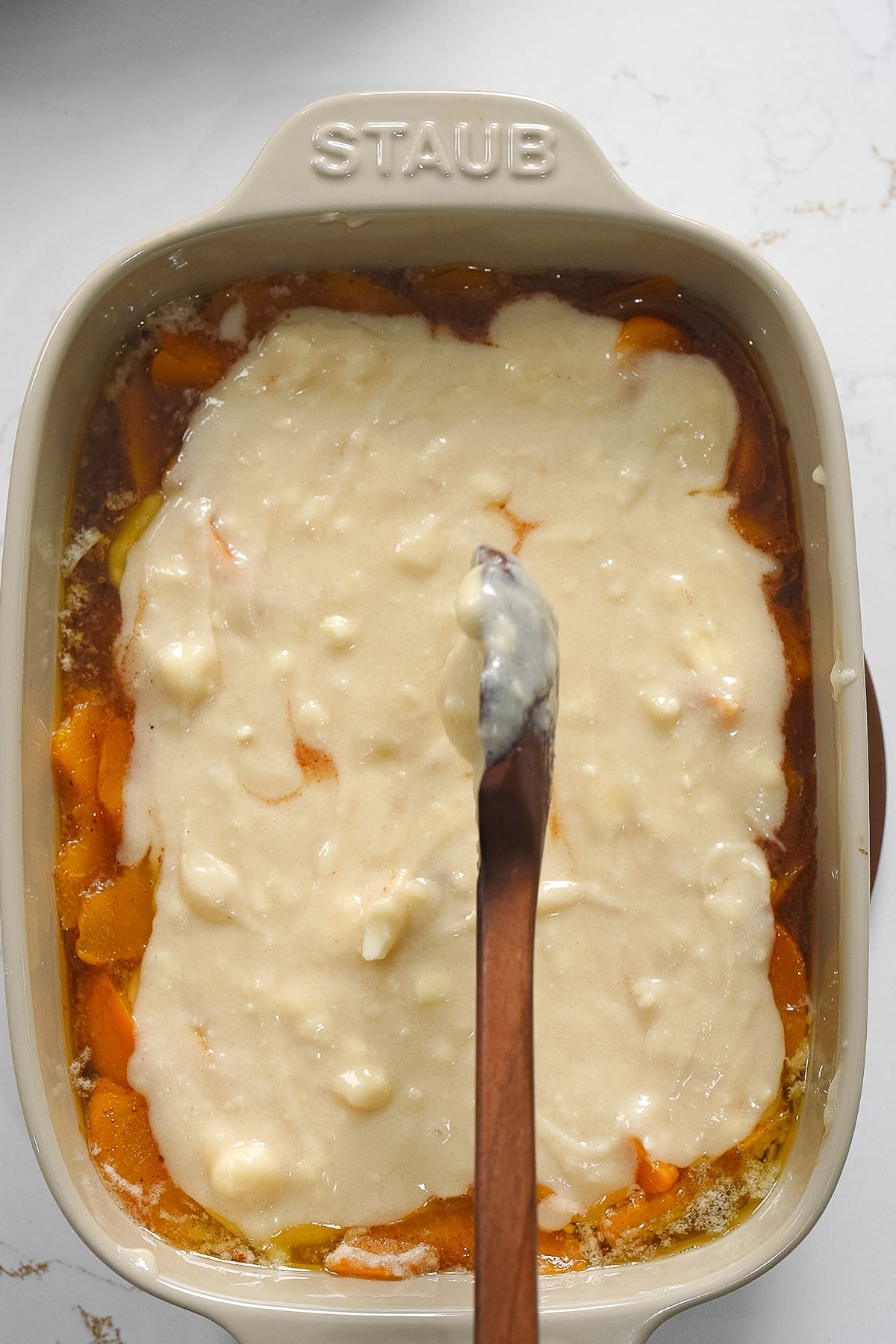 Putting wet biscuit dough on top of peaches in baking dish