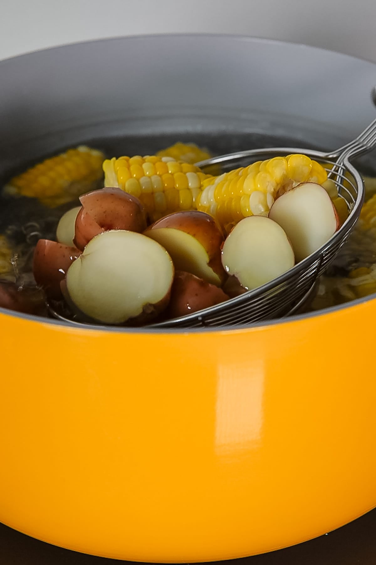potatoes and corn being boiled in pot and colander removing them from water