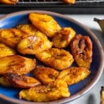 fried plantains on blue plate with plantains in rack in back