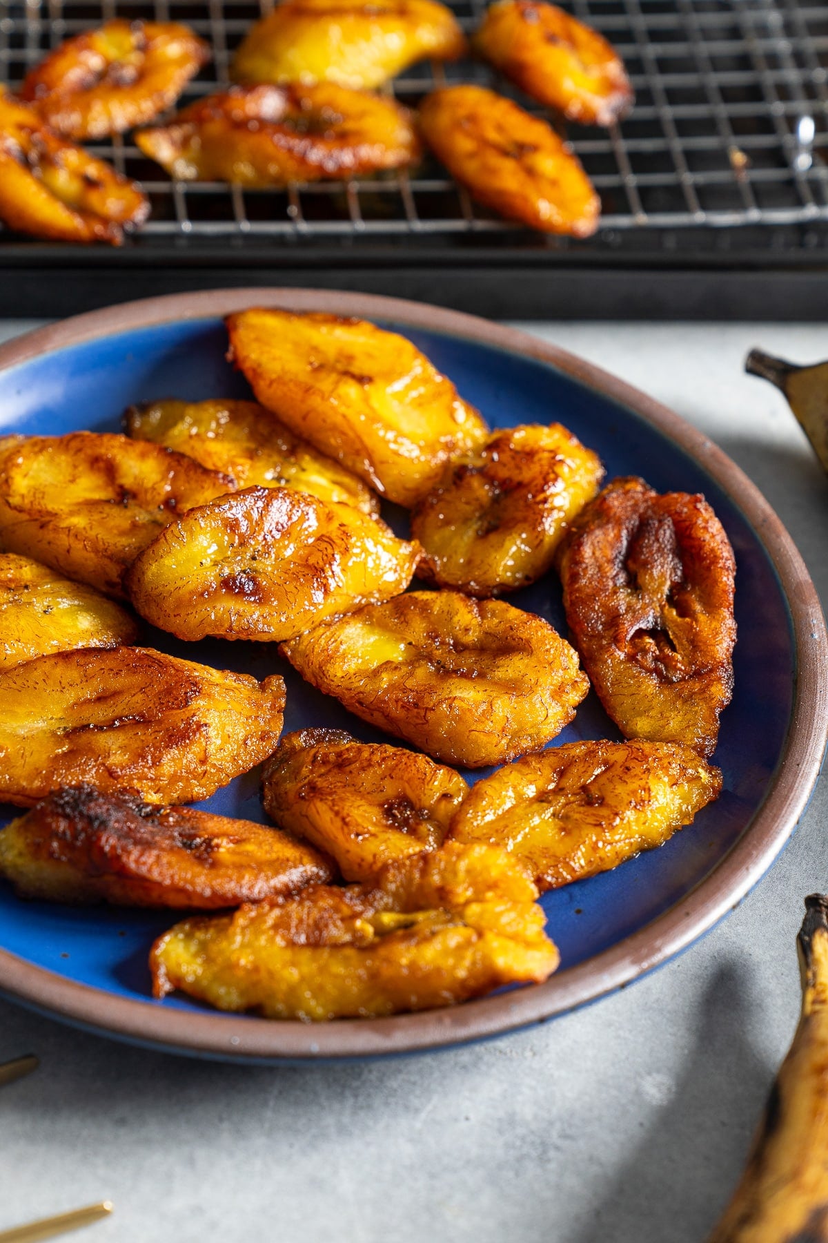 fried plantains on blue plate with plantains in rack in back