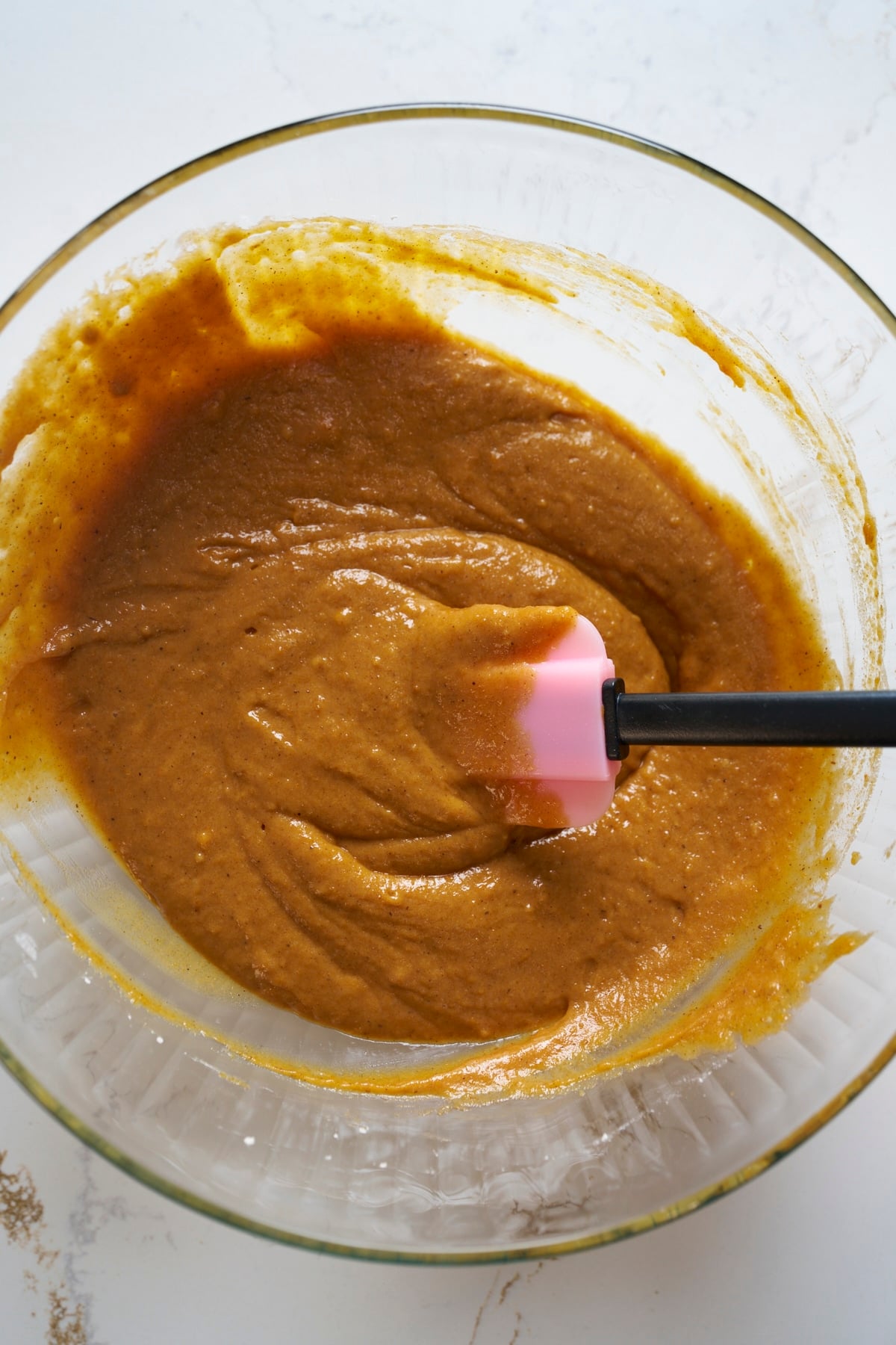 Thick spiced pumpkin bread batter folded together in a glass bowl with a spatula