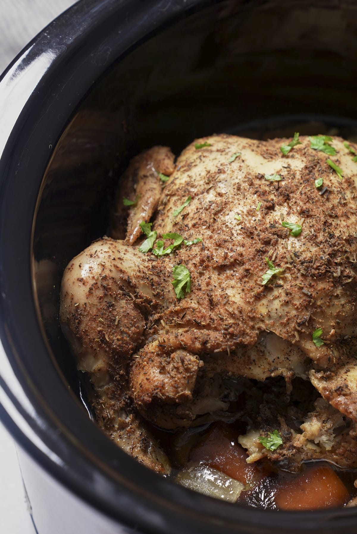 cooked whole chicken in slow cooker insert with parsley sprinkled on top, close up