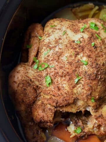 cooked whole chicken in slow cooker insert with parsley sprinkled on top