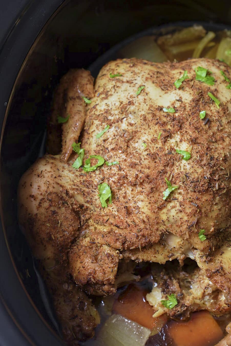 cooked whole chicken in slow cooker insert with parsley sprinkled on top