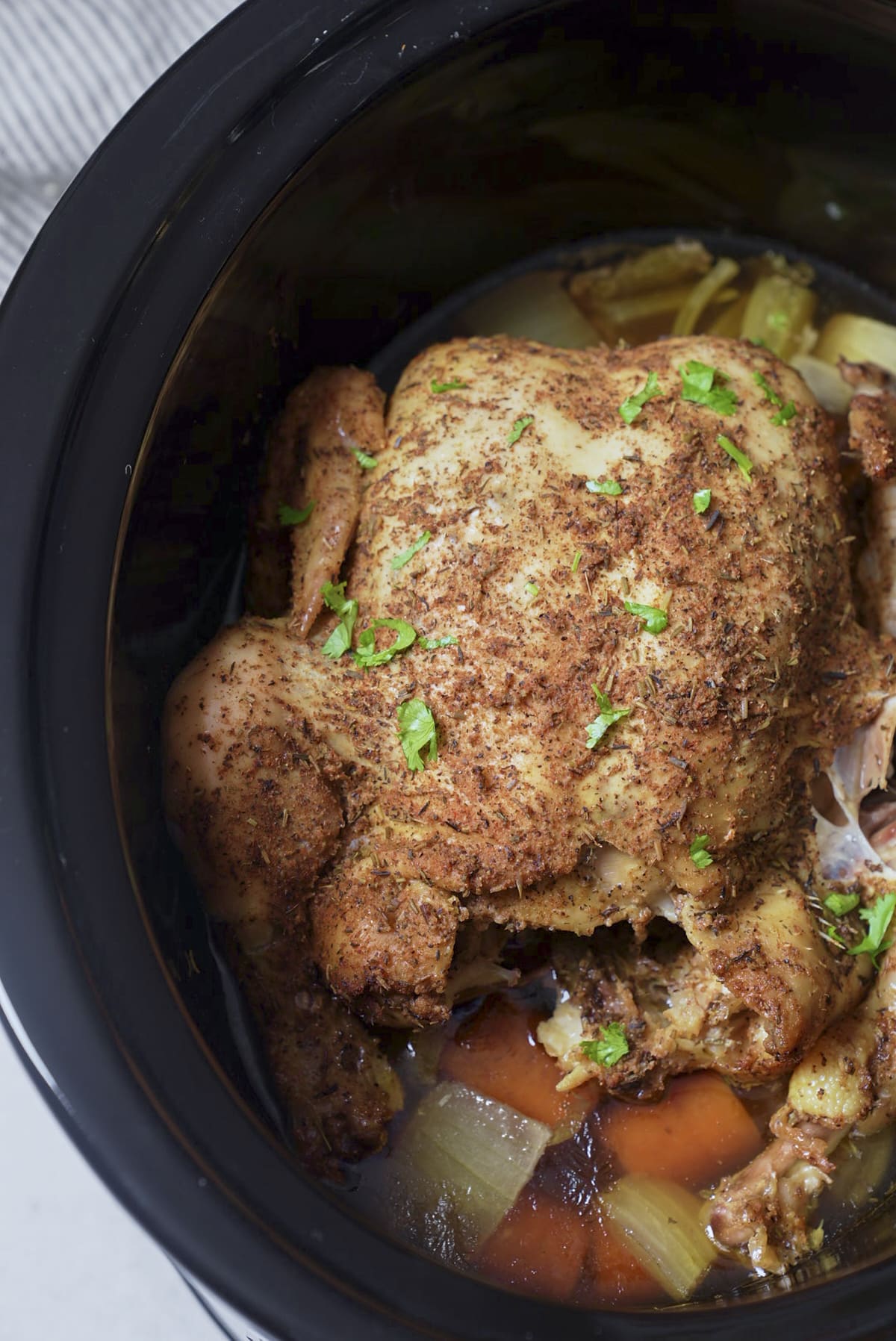cooked whole chicken in slow cooker insert with parsley sprinkled on top