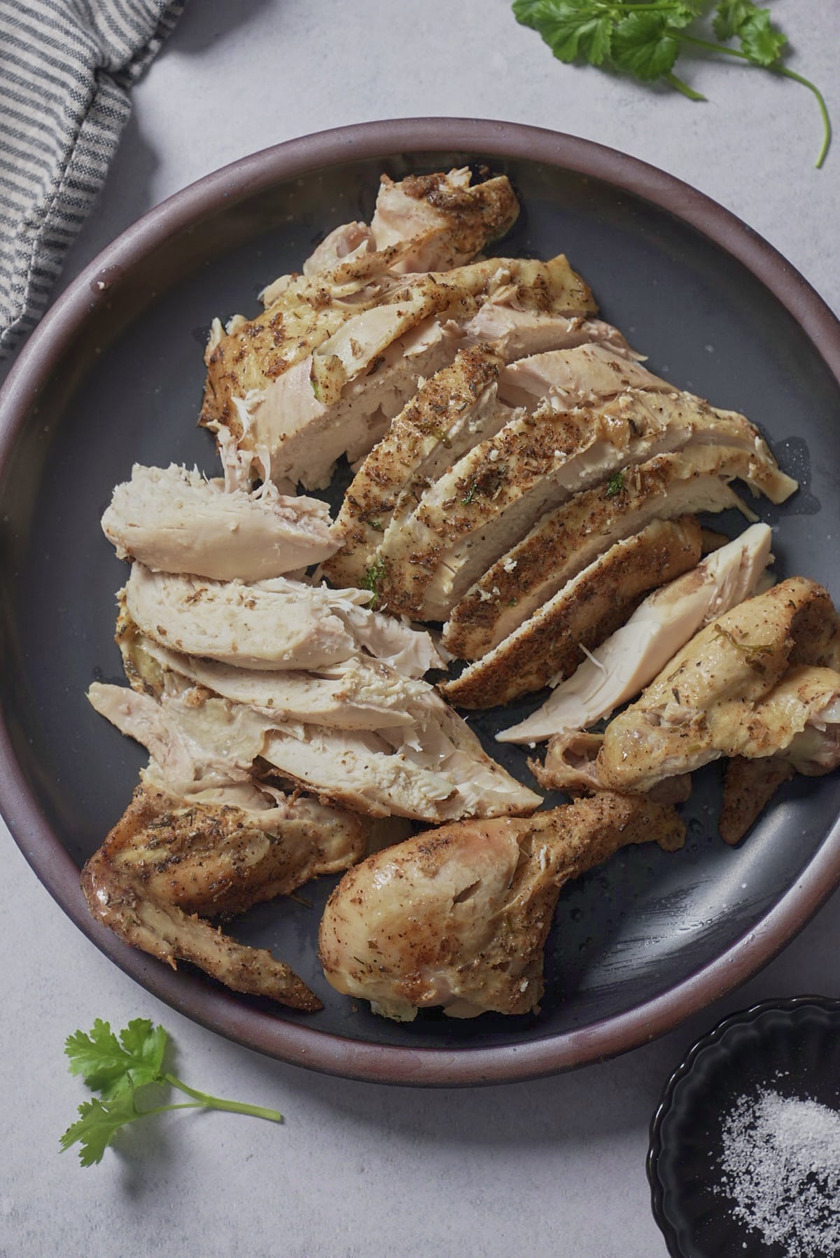 Carved slow cooker chicken breast slices, thigh, and drumstick arranged on a dark plate with fresh parsley.