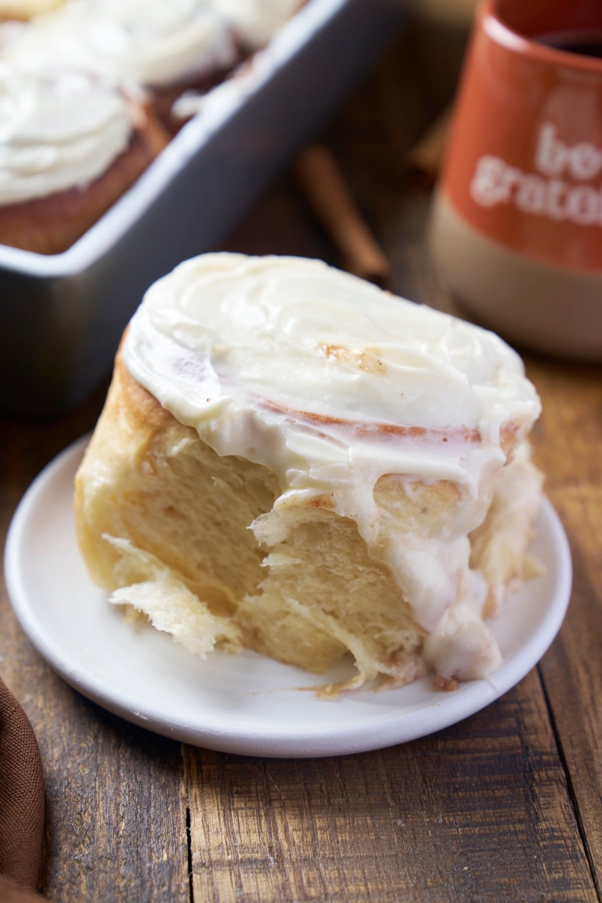 single cinamon roll on plate with coffee mug in background