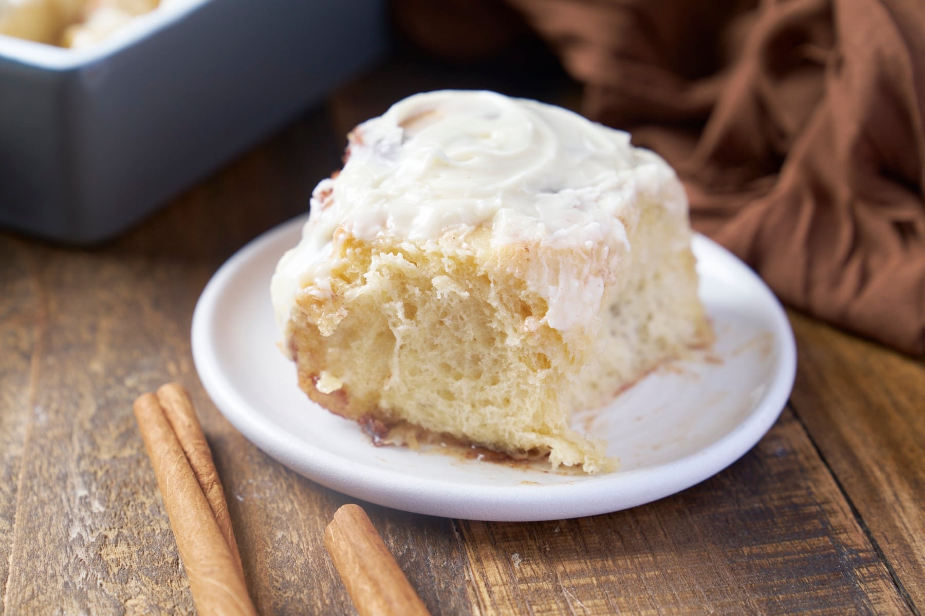 Homemade cinnamon roll made with heavy cream topped with cream cheese icing on a white plate.