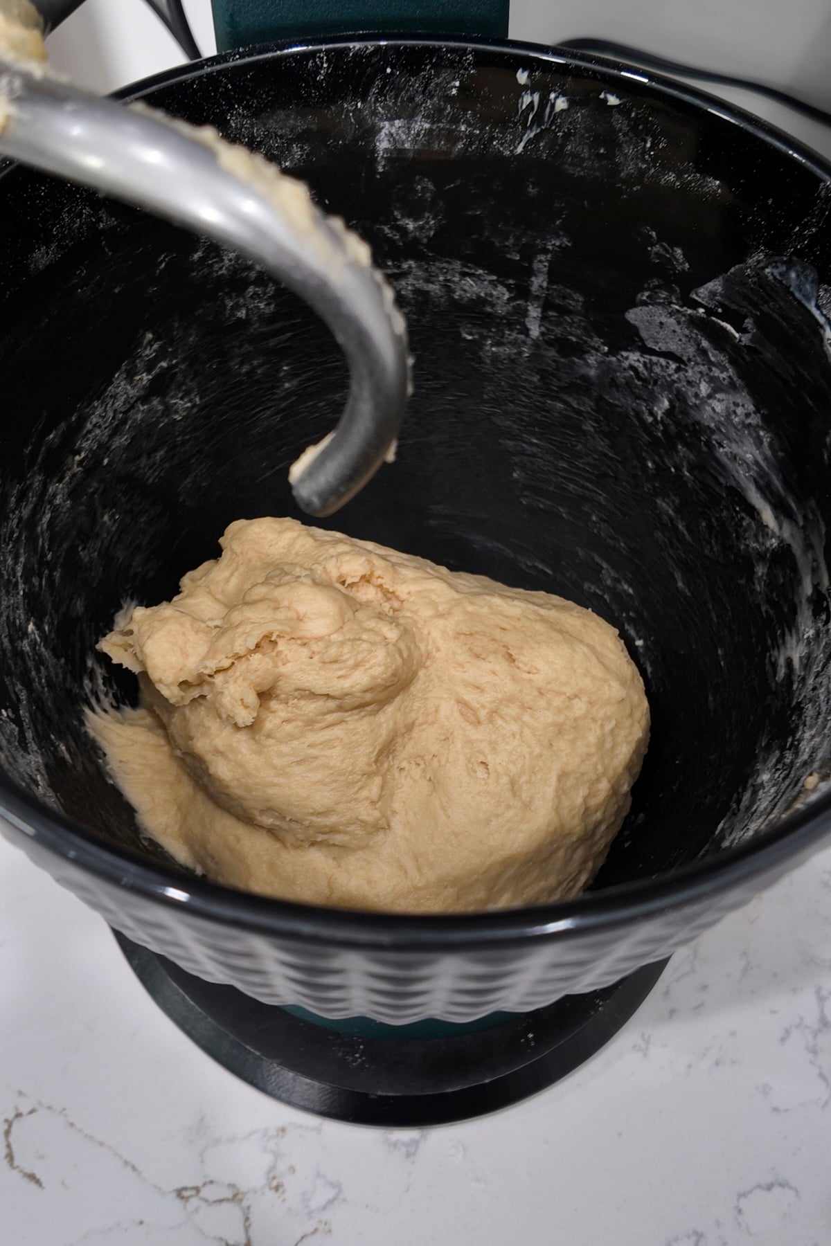 Homemade cinnamon roll dough kneaded smooth in a black stand mixer bowl.