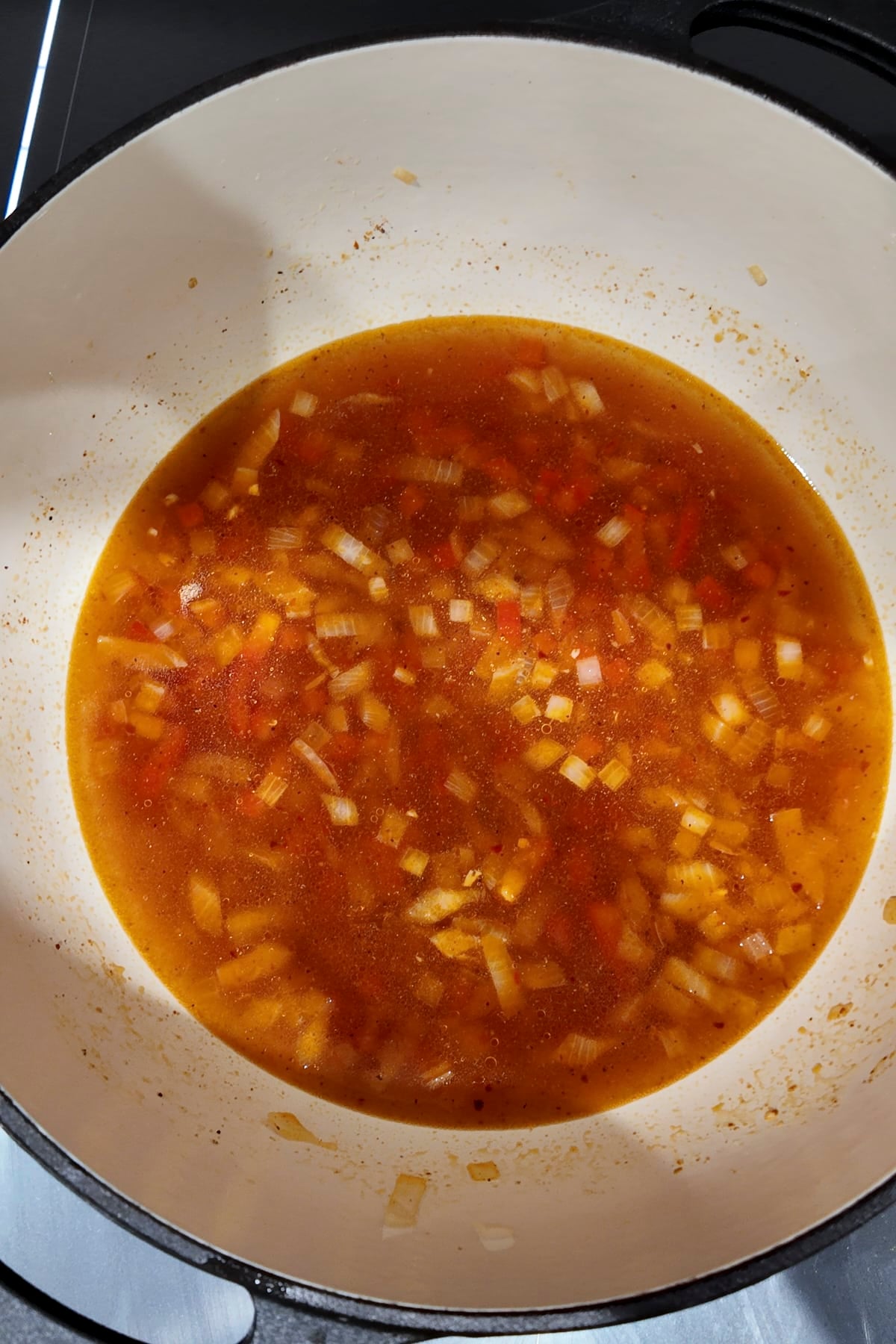 Amber vegetable broth poured into the pot, covering the softened onion and red bell pepper.
