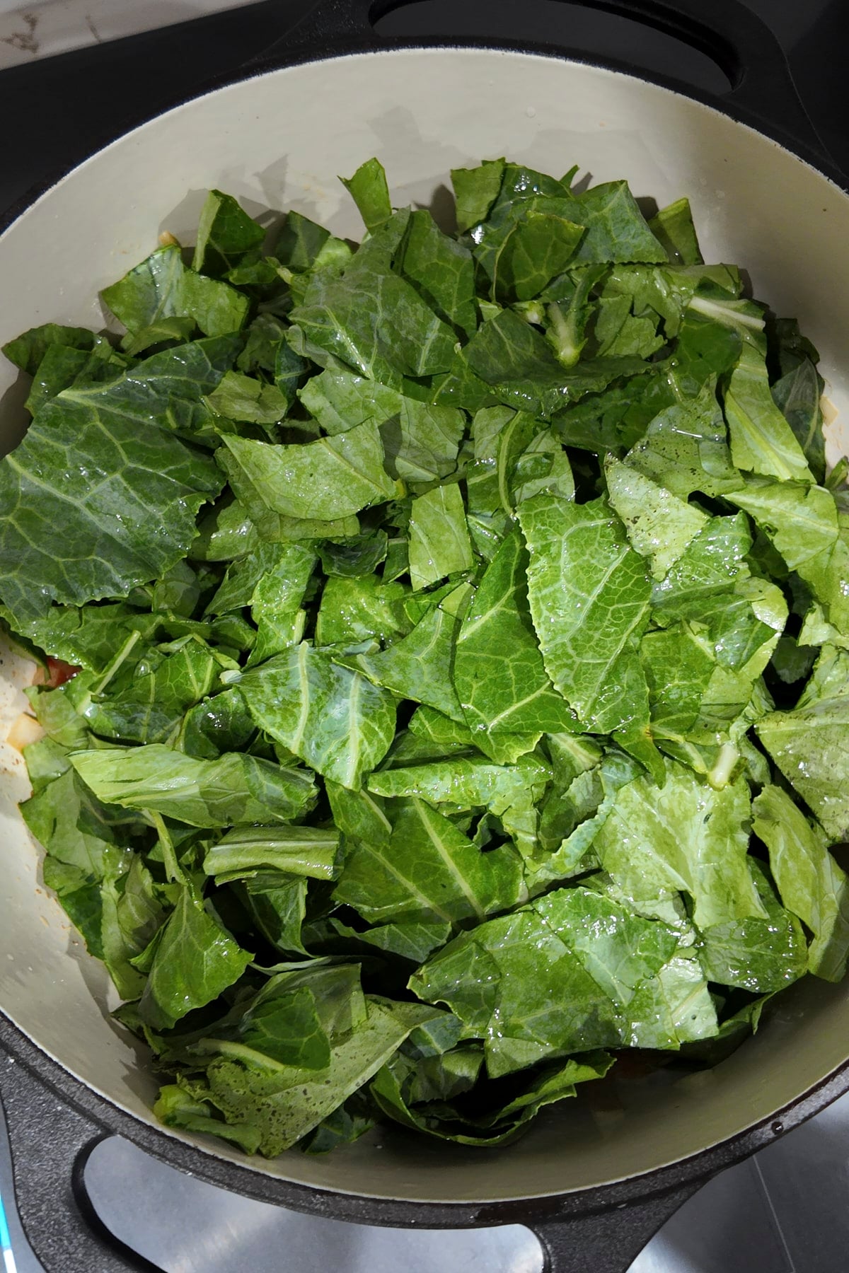 Raw chopped collard greens piled high in the pot on top of the broth and vegetables, before they have wilted.