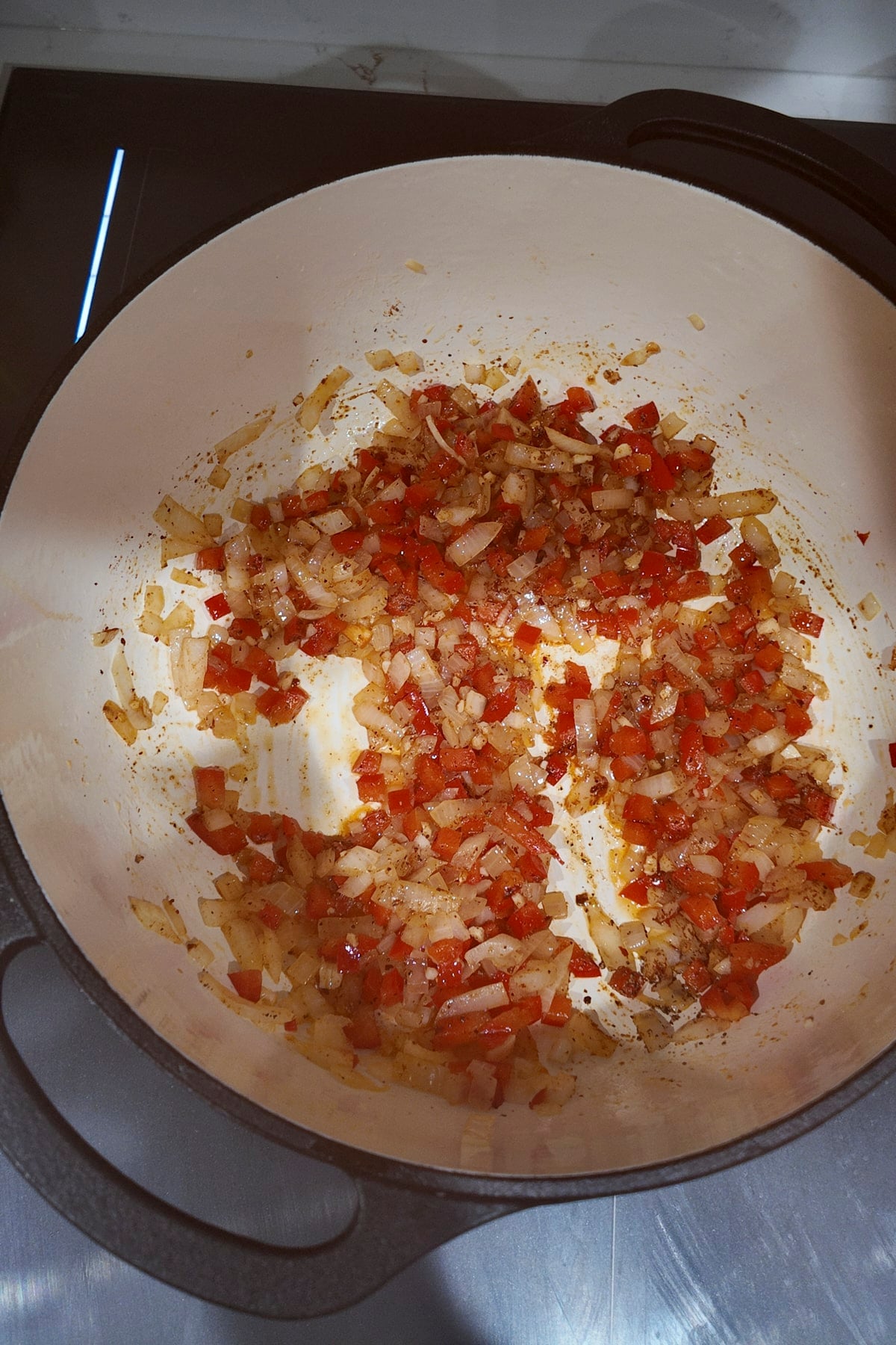 Diced onion, red bell pepper and minced garlic in a white enameled pot with smoked paprika and other ground spices stirred through and lightly browned.