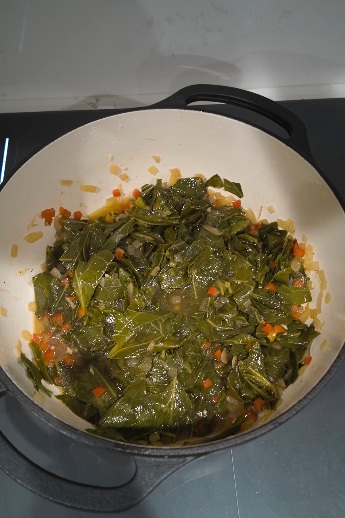 Collard greens wilted down into the broth in the pot, with pieces of onion and red bell pepper scattered through the leaves.