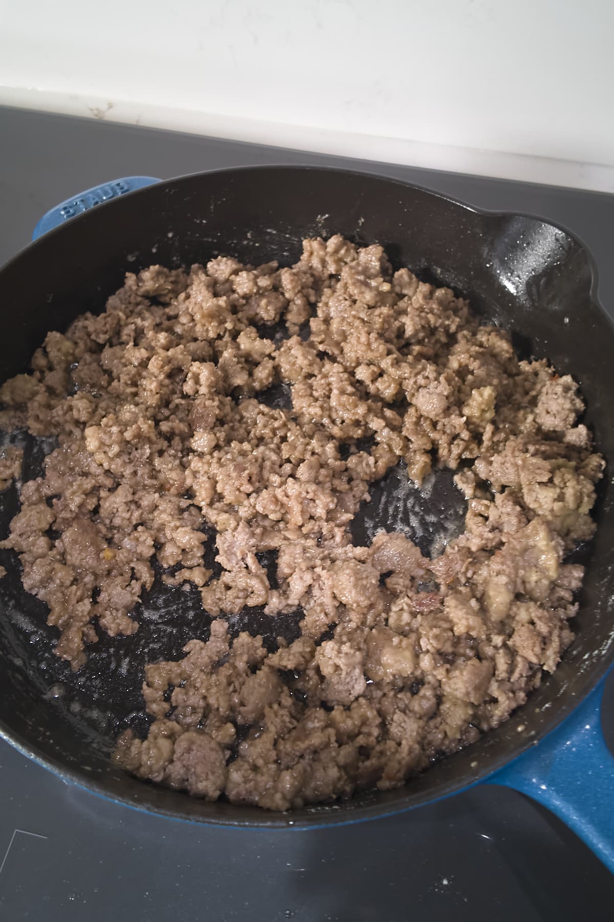 Browned sausage crumbles evenly coated in flour in a cast iron skillet.