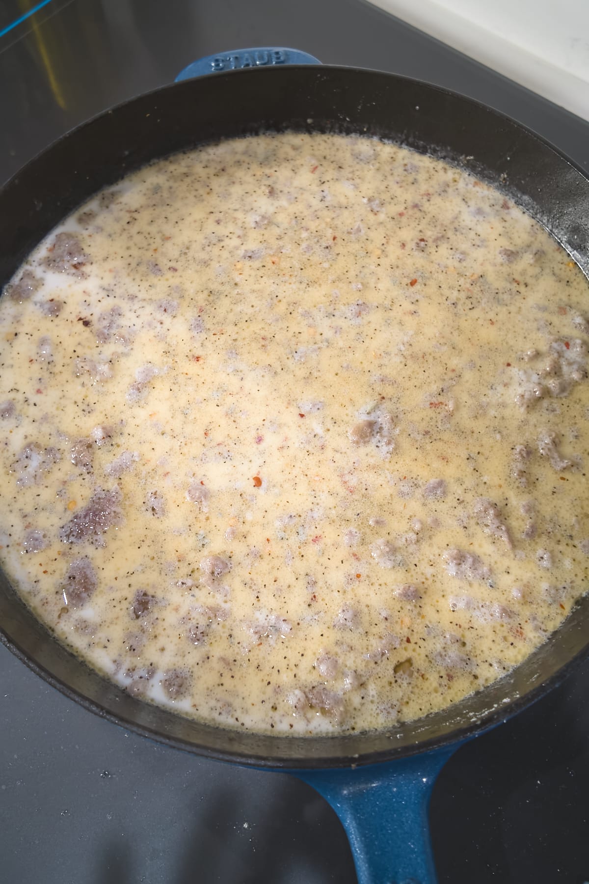 Milk poured over the flour-coated sausage in a cast iron skillet, still thin before simmering.