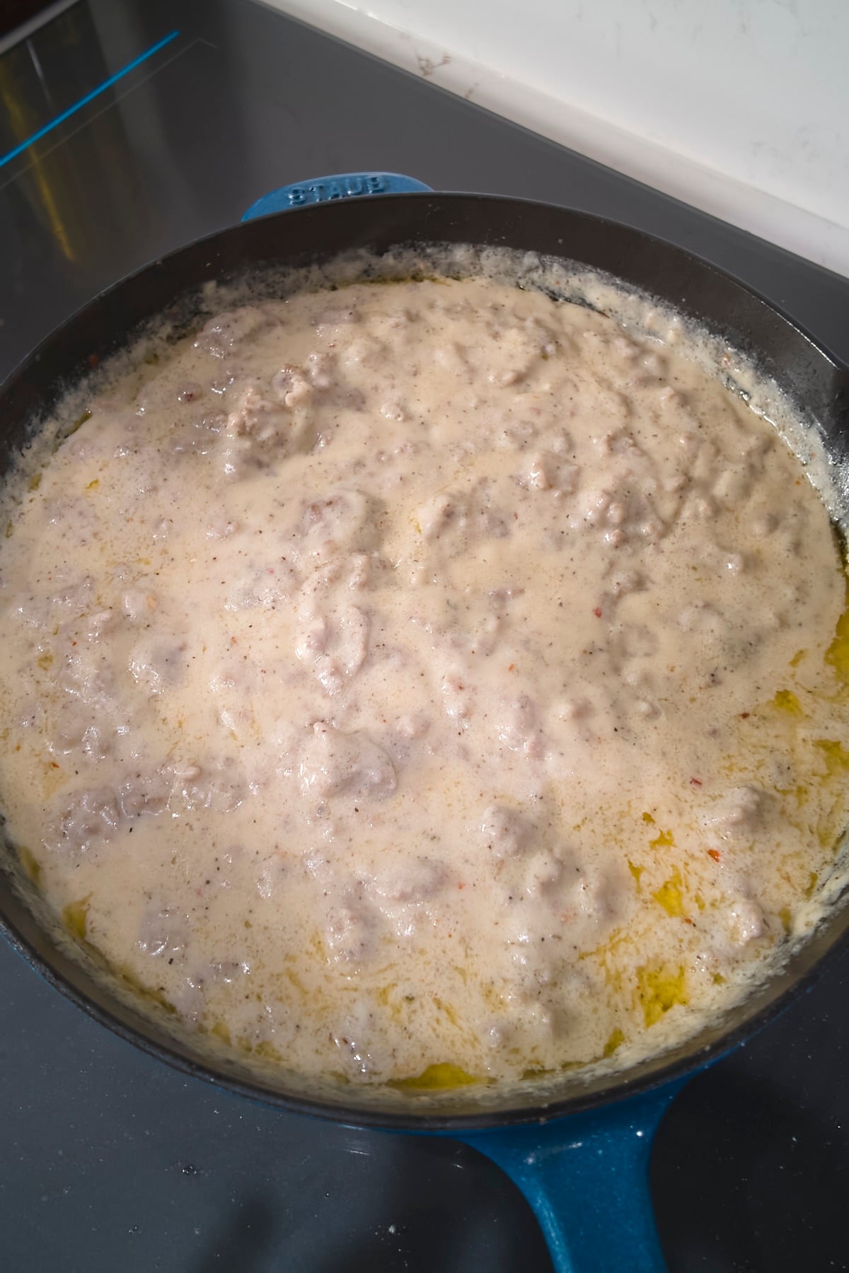 Sausage gravy thickened after simmering in a cast iron skillet, flecked with seasonings.