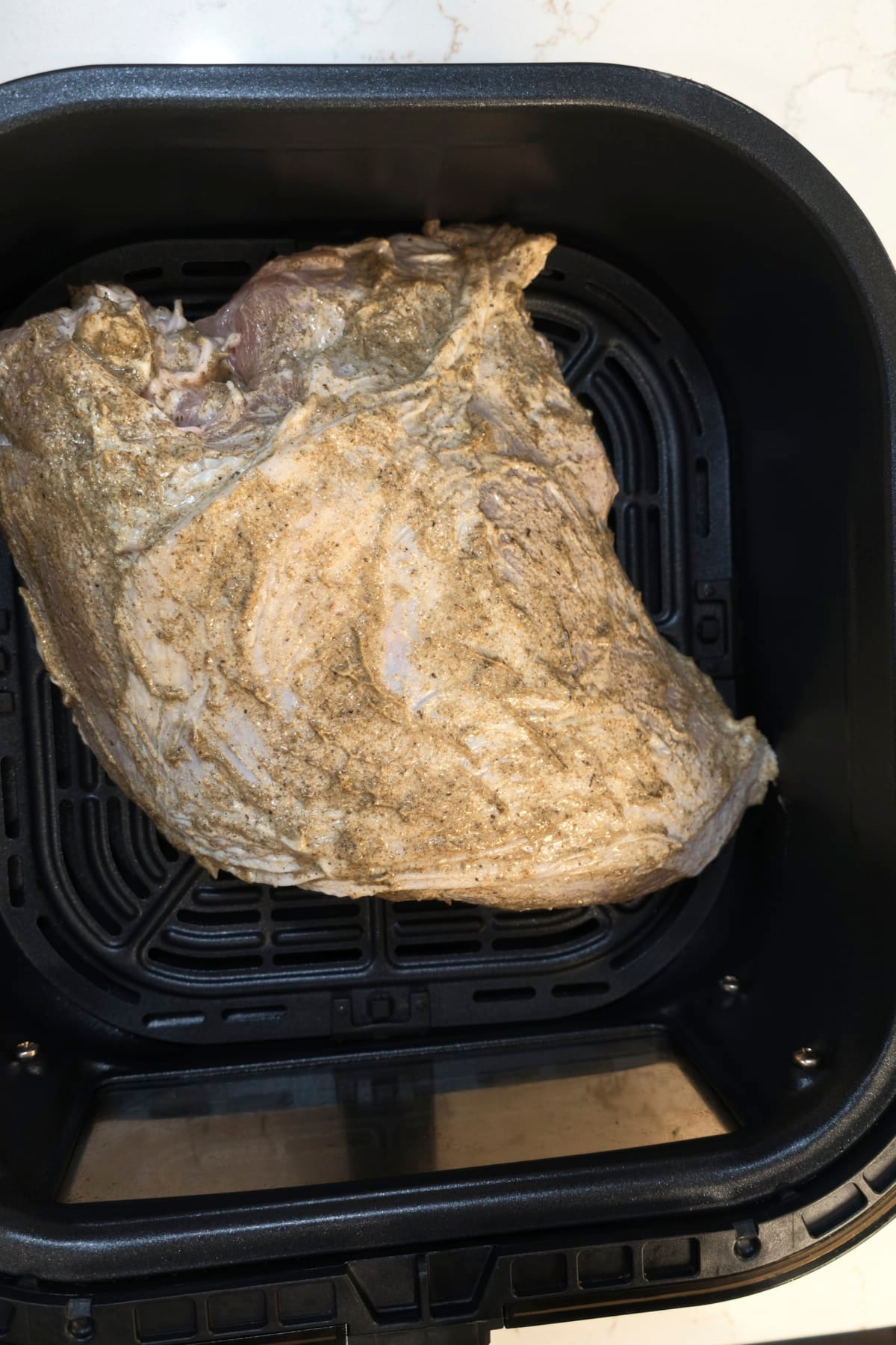 Raw turkey breast coated all over in seasoned mayo rub, skin side up in the air fryer basket