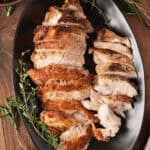 Sliced turkey breast with golden, seasoned skin on a black platter, with gravy and collard greens on the side
