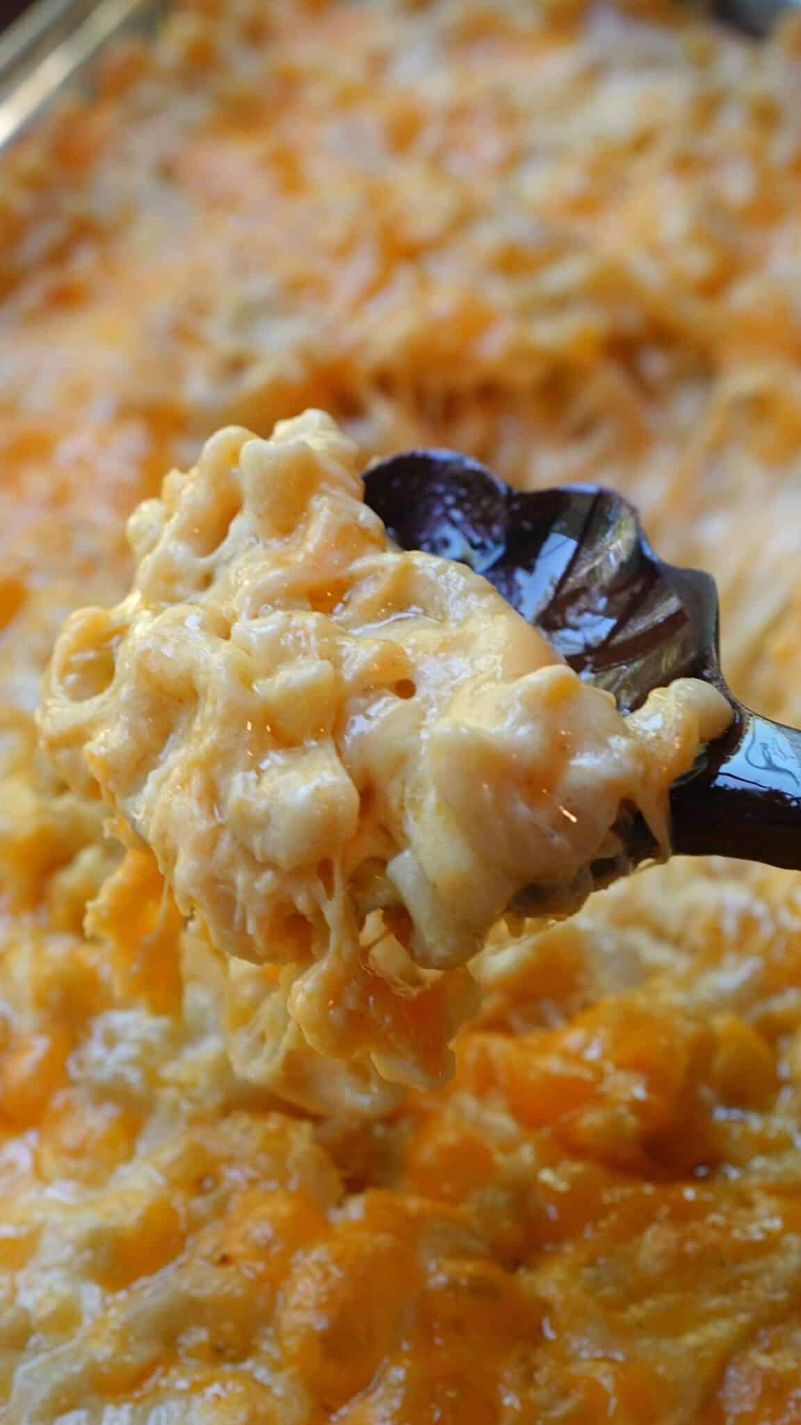 A spoonful of baked mac and cheese held above the dish, showing the creamy, cheesy pasta inside.