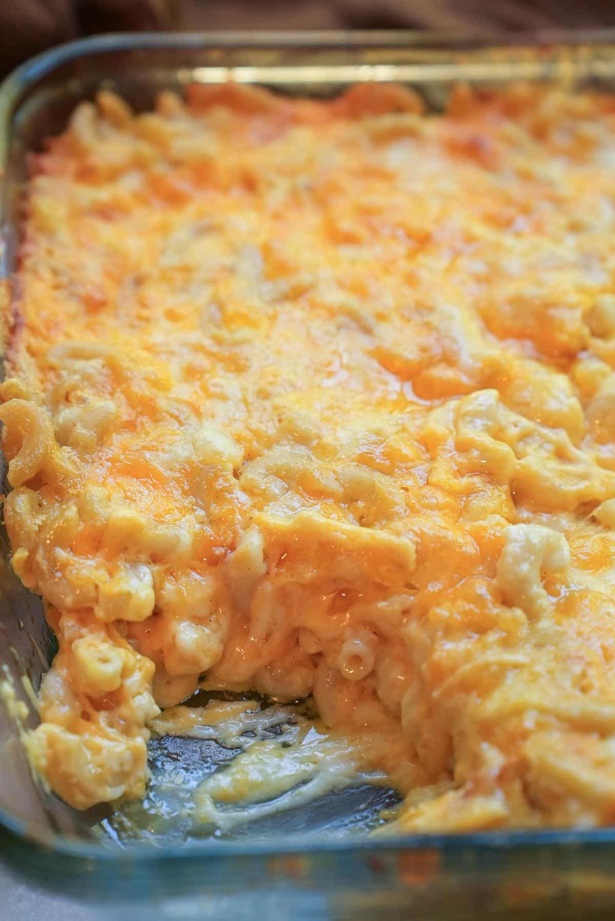 Baked mac and cheese in a glass dish with a corner scooped out, showing the creamy inside under the browned cheese top.