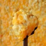 A serving spoon lifting a creamy scoop of mac and cheese from the baking dish.