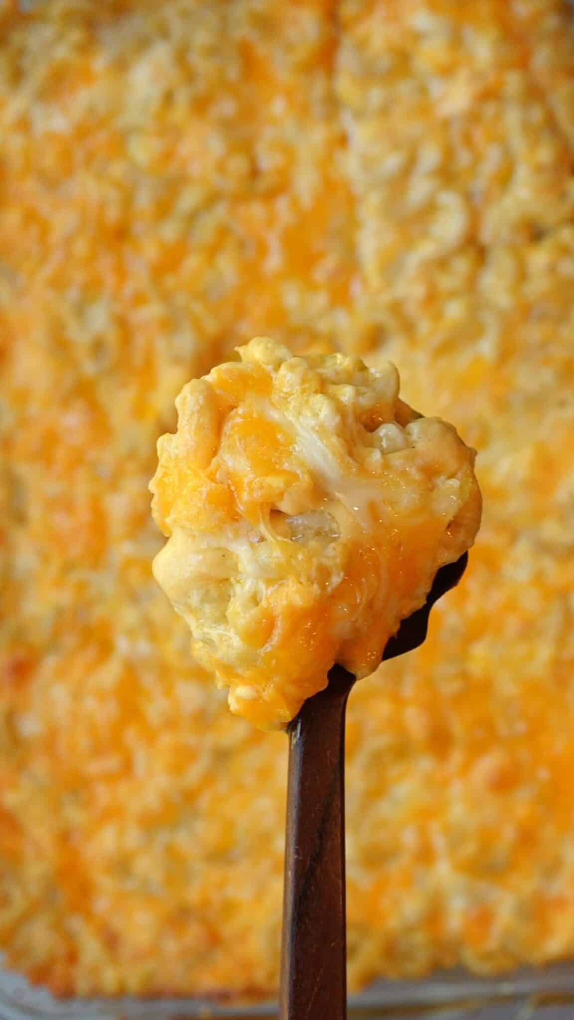 A serving spoon lifting a creamy scoop of mac and cheese from the baking dish.