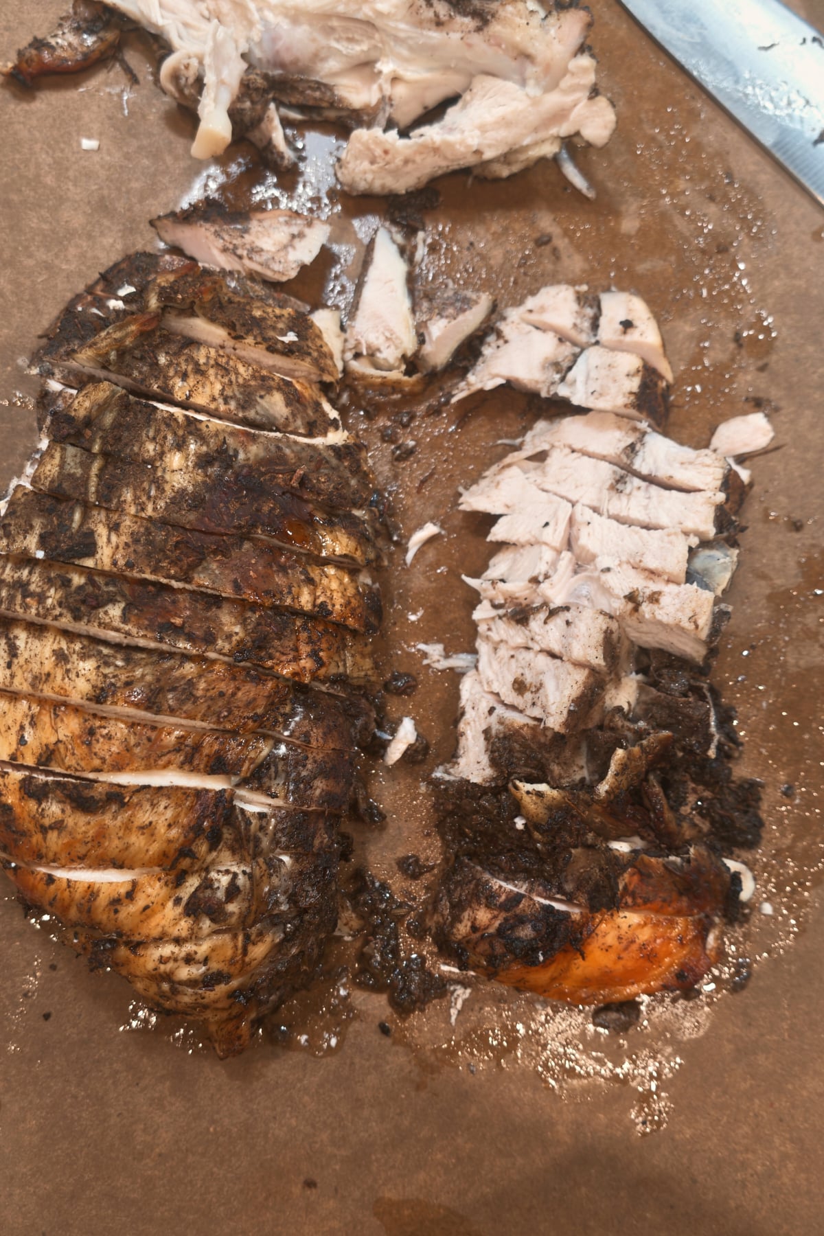 Roasted jerk turkey breast on a cutting board, the meat taken off the bone and sliced, with the bone set aside.