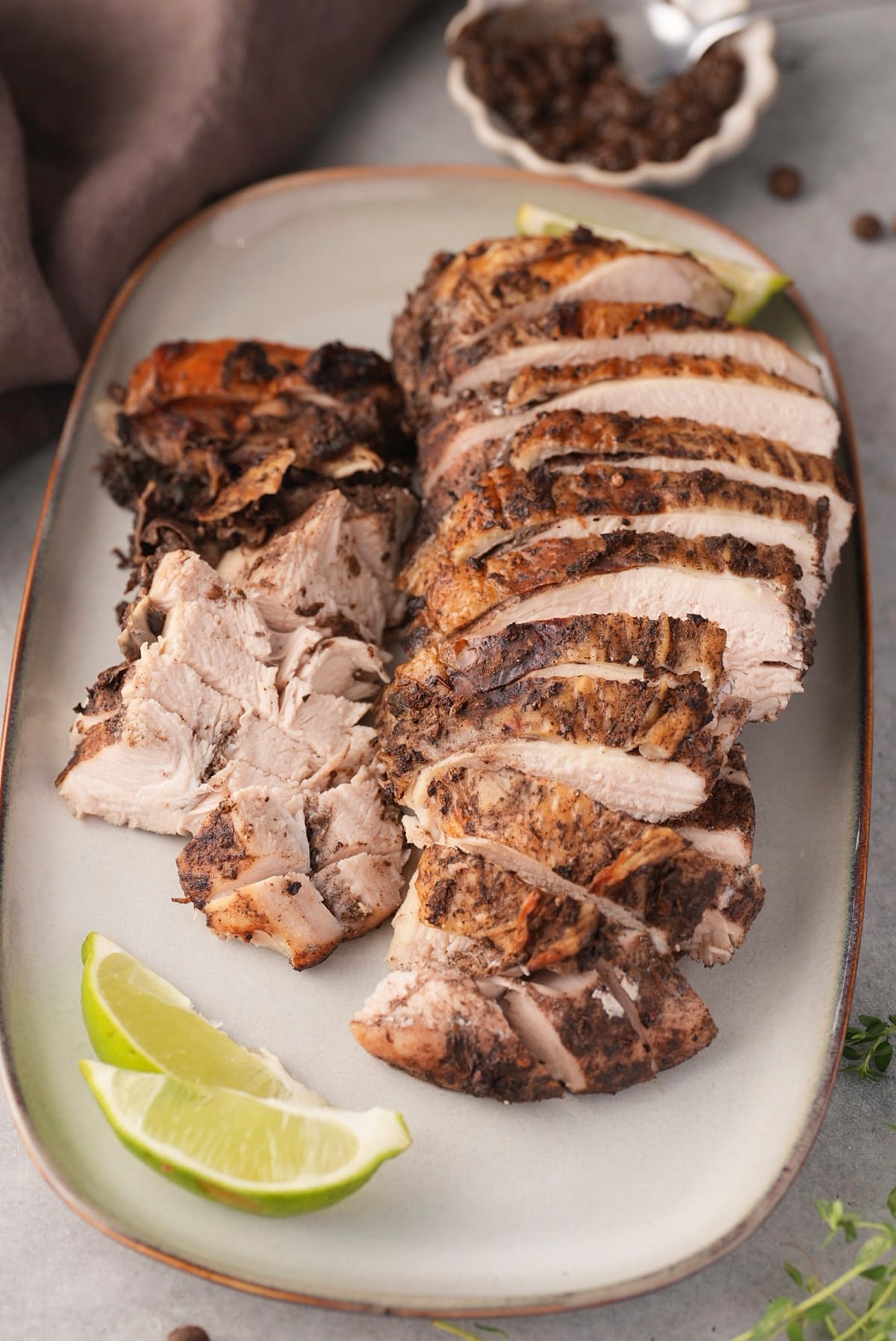 Overhead view of sliced jerk turkey breast on a platter with lime wedges.