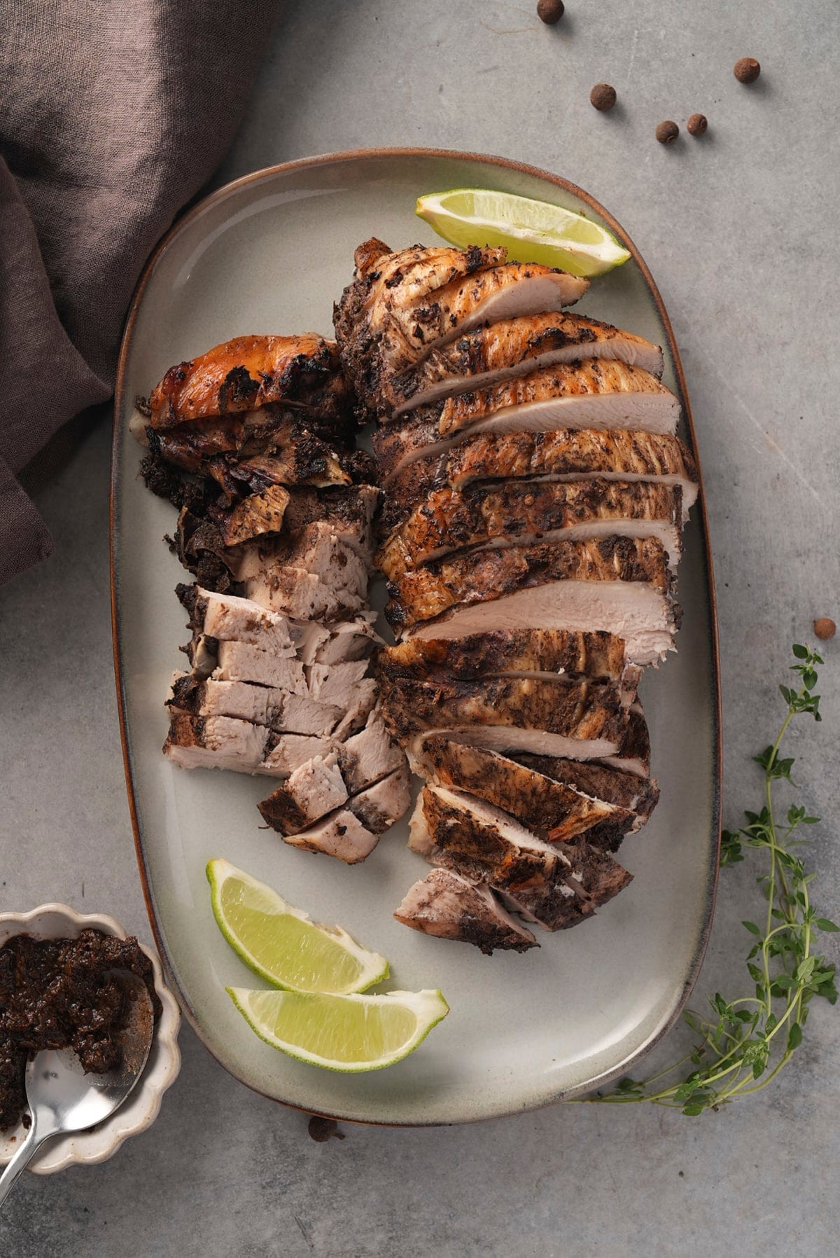 Carved jerk turkey on a platter with lime wedges, next to a small dish of jerk seasoning.