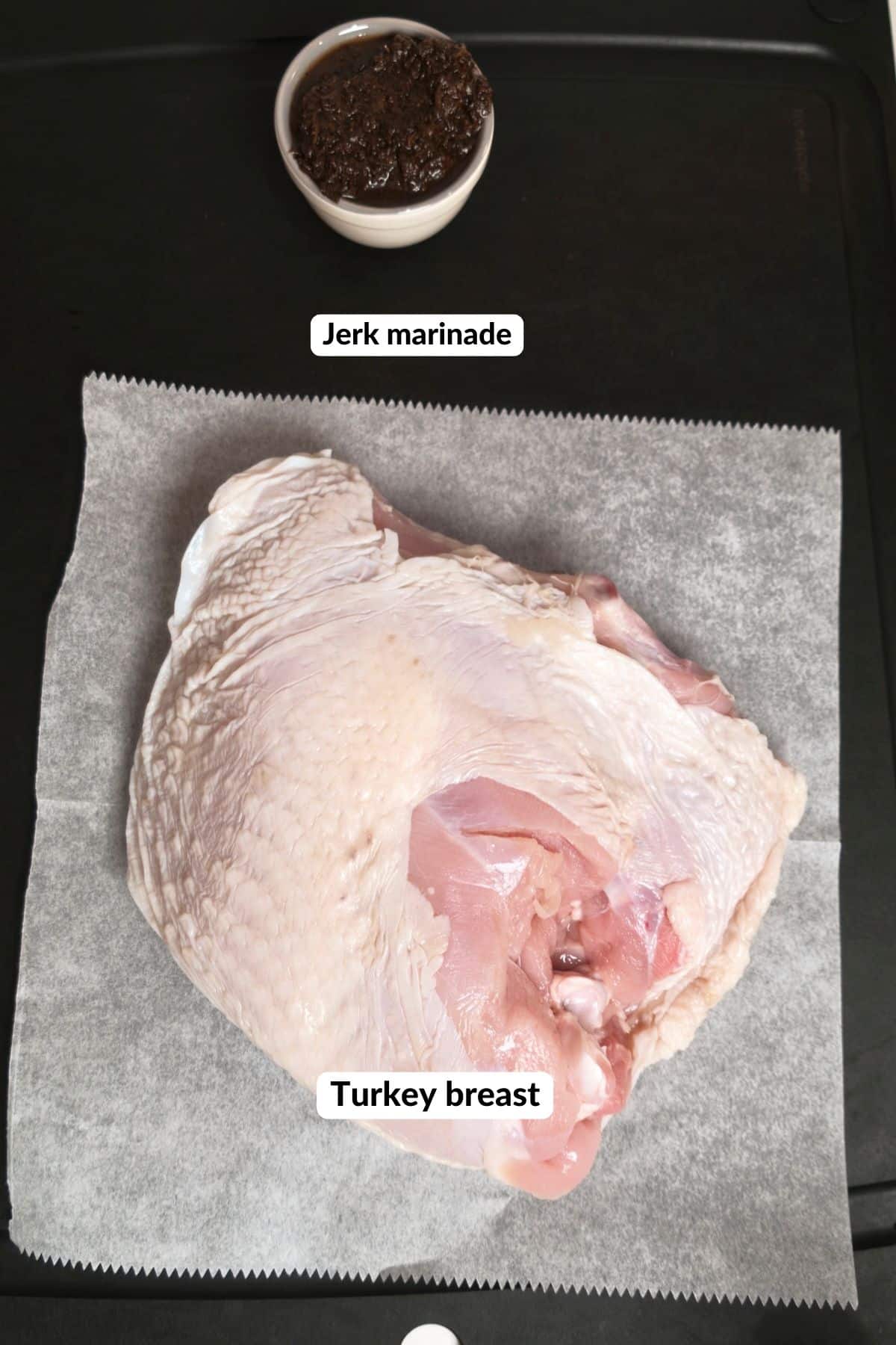 A raw bone-in turkey breast on parchment next to a small bowl of jerk marinade, each with a label.