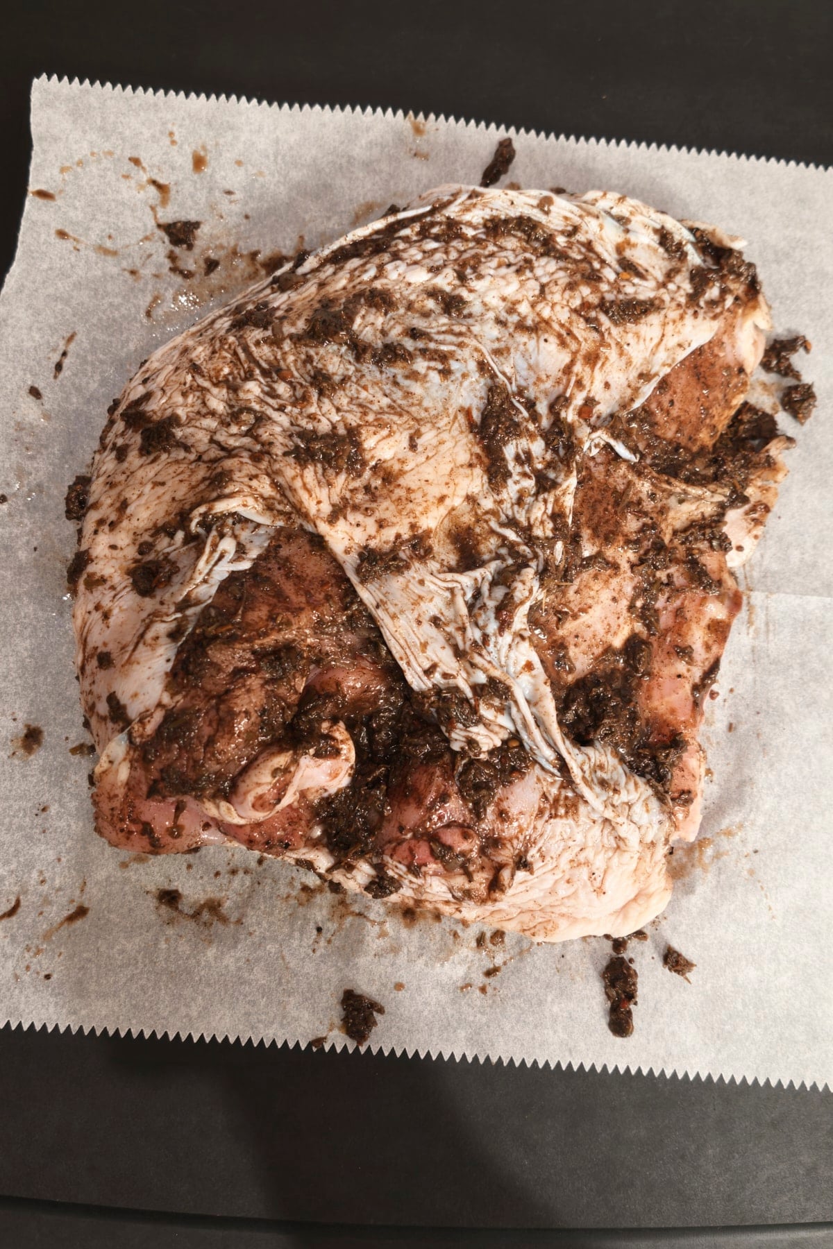 Raw turkey breast coated all over in jerk paste on parchment, ready to marinate.