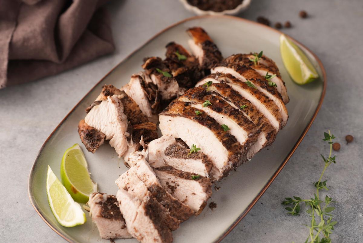Platter of sliced jerk turkey breast with lime wedges and sprigs of thyme.