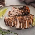 Sliced jerk turkey breast on an oval platter with lime wedges and fresh thyme.