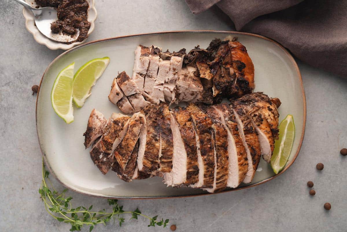 Sliced jerk turkey breast on an oval platter with lime wedges and fresh thyme.