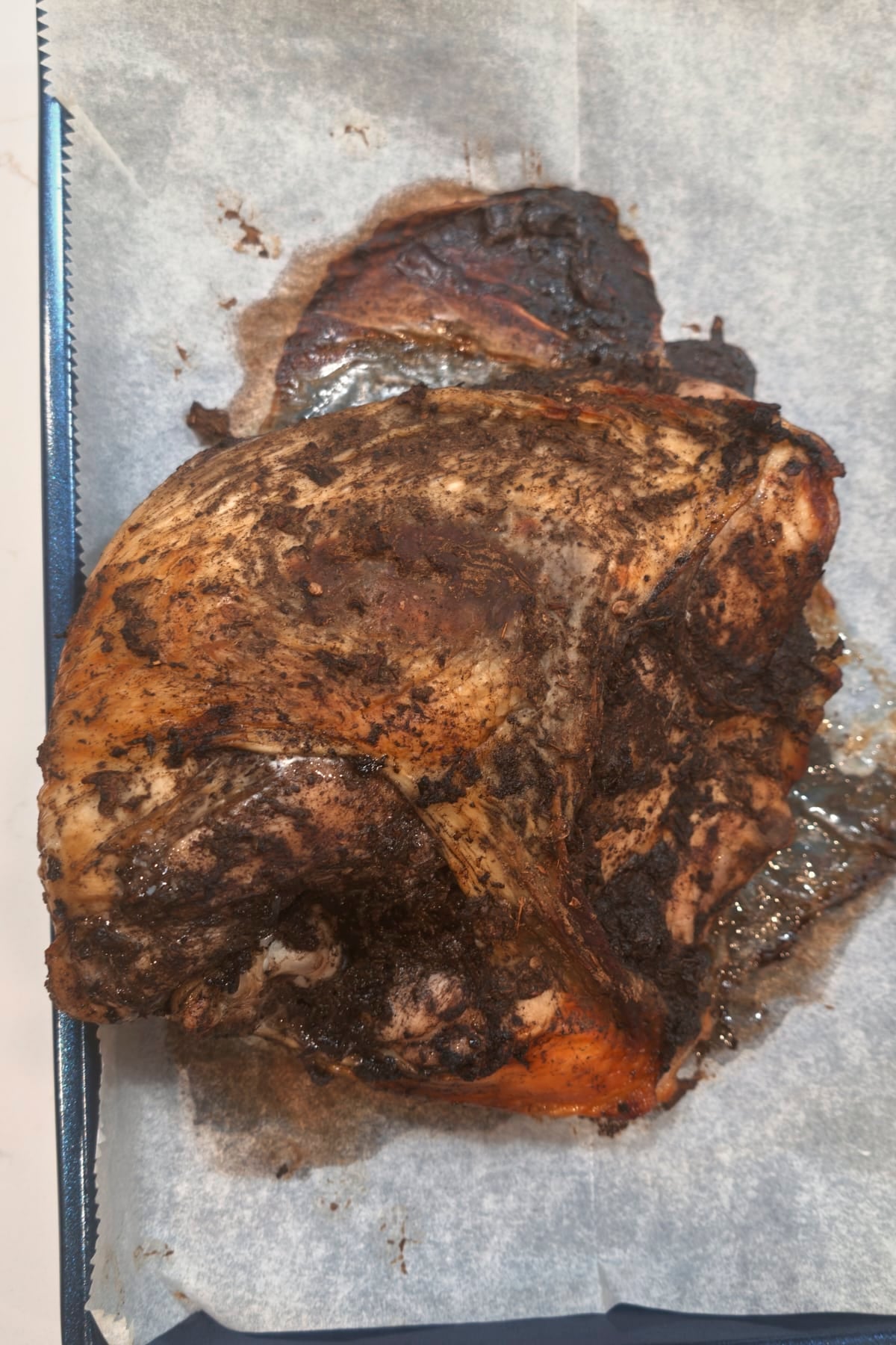 Whole jerk turkey breast after roasting, dark and crisp on top, on a parchment-lined pan.